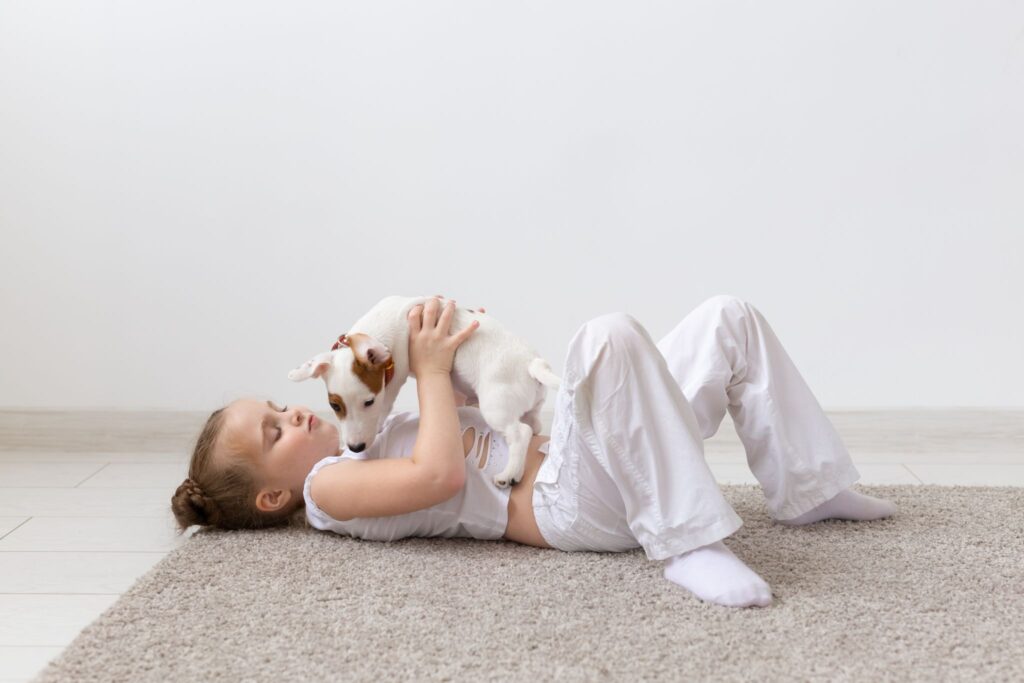 Young girl lying on the floor playing with a small puppy, illustrating cognitive, emotional, and developmental benefits of having a dog for children